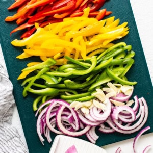 Sliced peppers and onions on a cutting board.