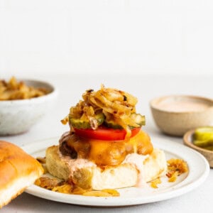 A homemade burger with onions and pickles on a plate.