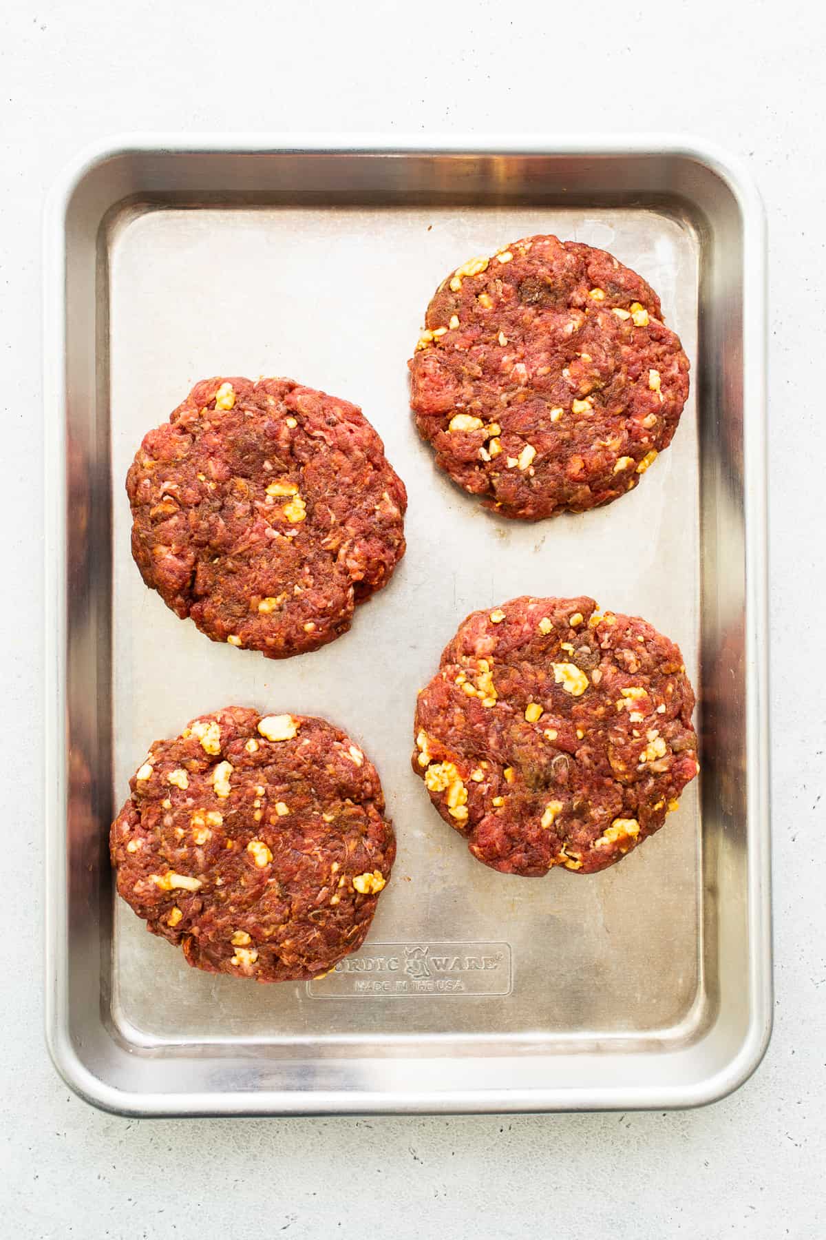 Homemade burger patties on a baking sheet.