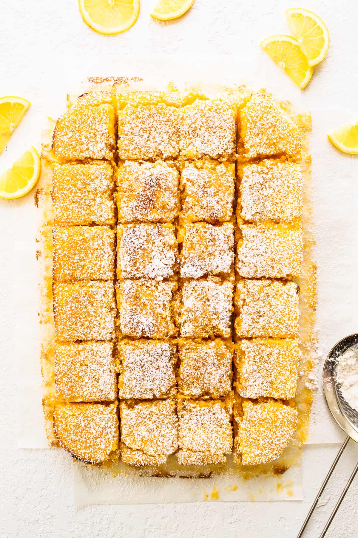 lemon bars on cutting board with lemon wedges.