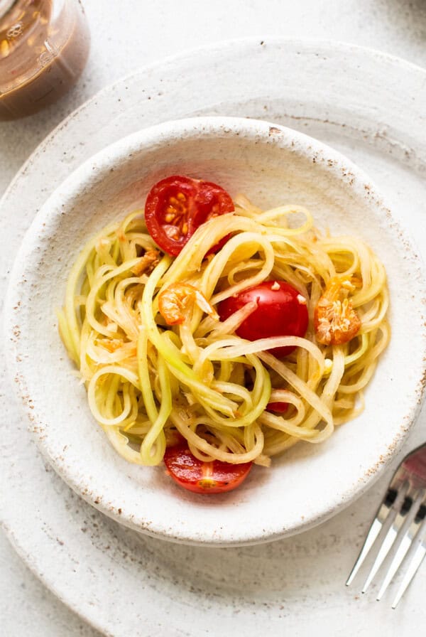 A plate of spaghetti with tomatoes and basil, topped with papaya salad.