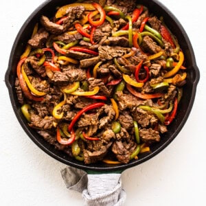 Beef enchilada in a skillet with peppers and onions.