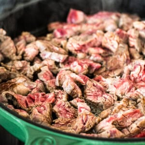 A green frying pan with meat in it.