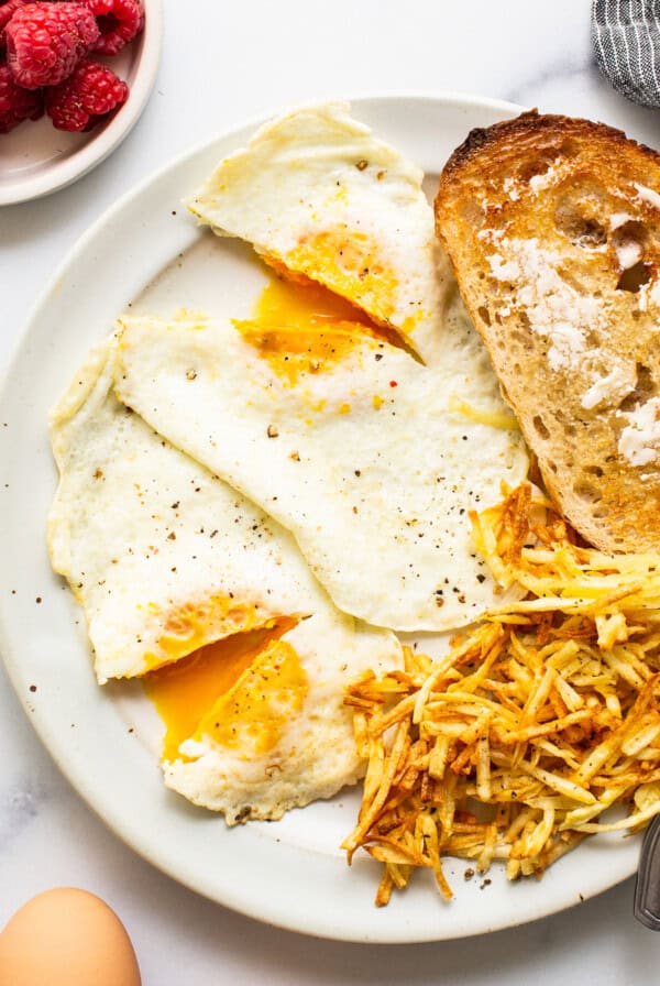 A plate with over medium eggs and toast, garnished with raspberries.