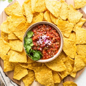 Nachos with salsa on a wooden cutting board.