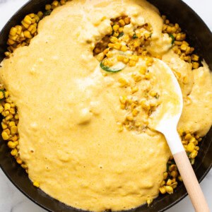 Corn on the cob in a skillet with a wooden spoon.