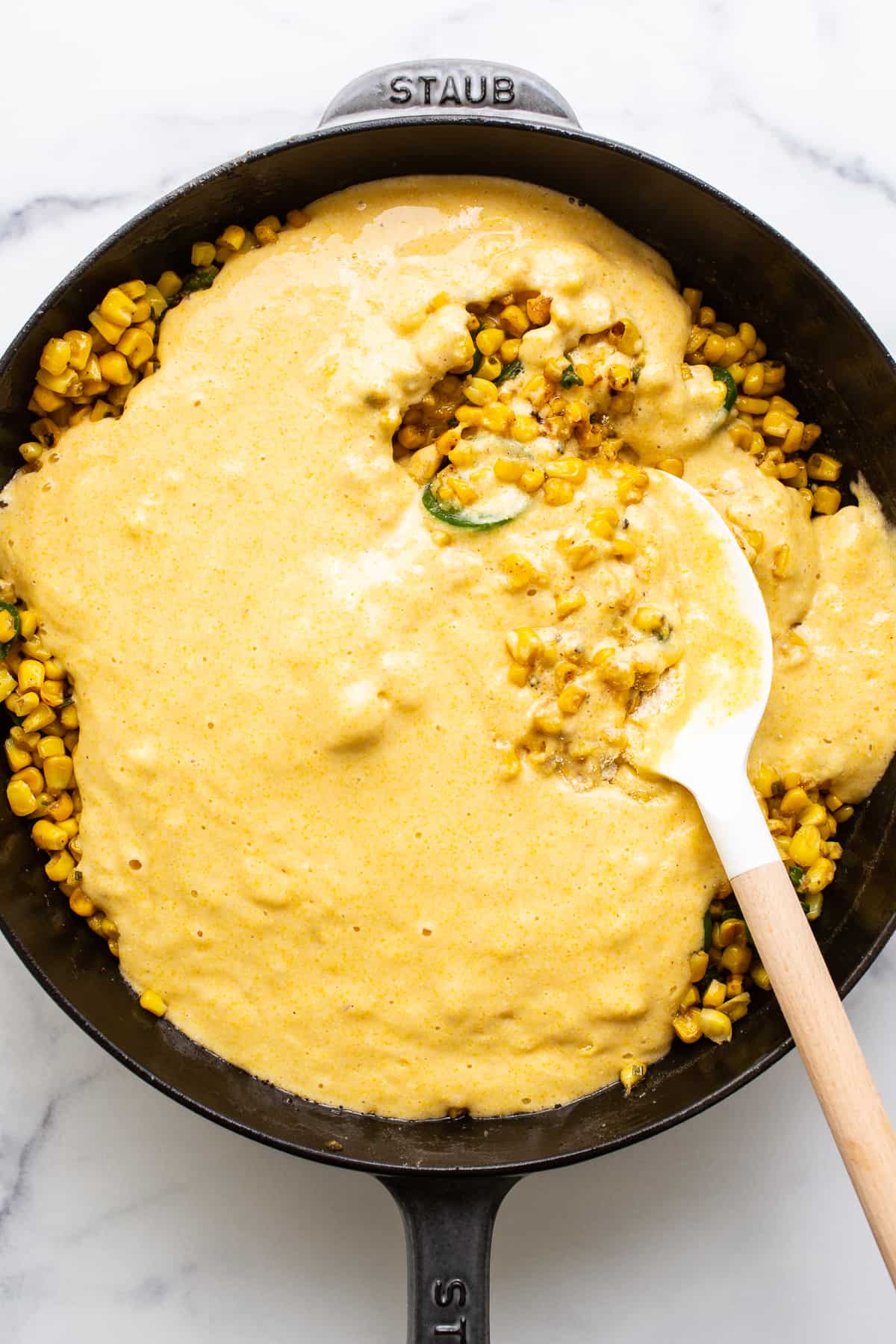 Cornbread mix in a cast iron skillet with corn and sliced jalapenos.