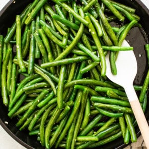 Green beans in a skillet with a wooden spoon.