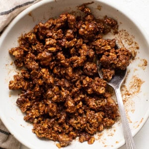 Granola in a white bowl with a spoon.