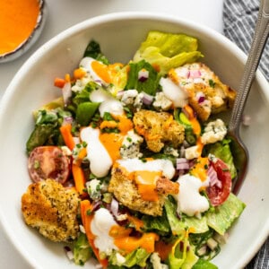 A white bowl with a salad and dressing on it.