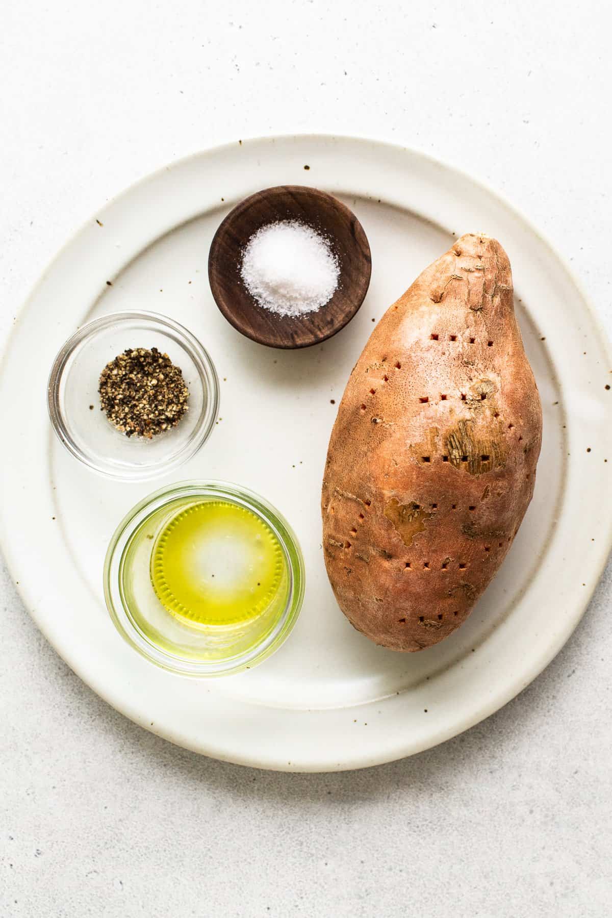 A sweet potato, salt, pepper, and oil on a plate. 