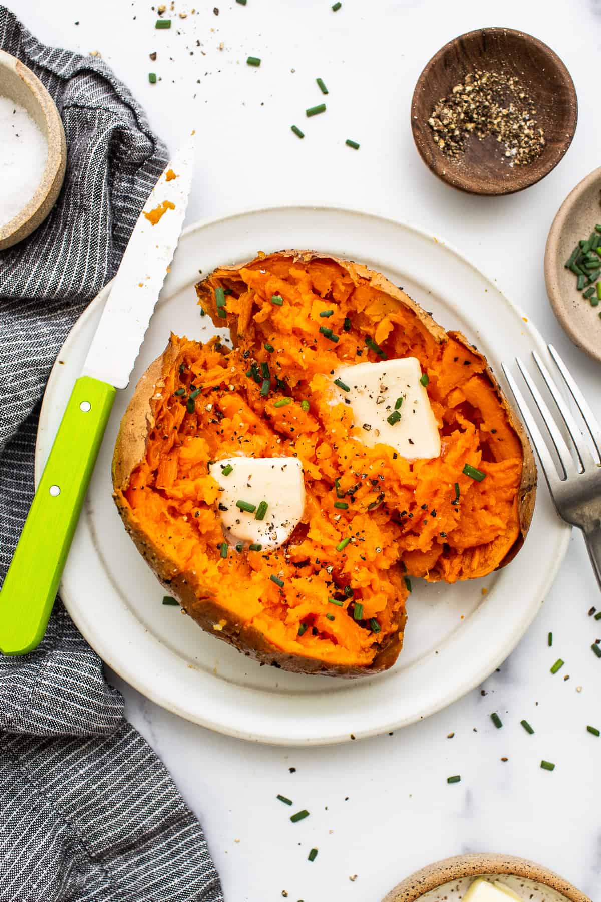 Baked sweet potato on a plate topped with butter.