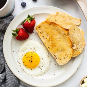 A sunny side up egg on a plate with salt and pepper.