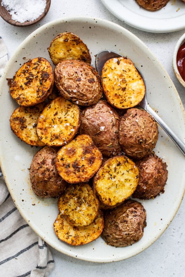 Roasted potatoes on a plate with ketchup and salt.