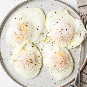 Four fried eggs on a plate with a napkin.