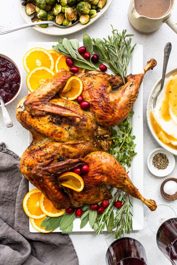 Spatchcock turkey with brussels sprouts and oranges on a white plate.