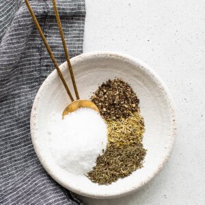 A white bowl with salt, pepper, and herbs.