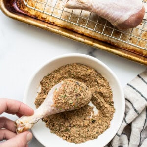 A person is sprinkling seasoning on a chicken wing.