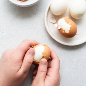 A person peeling an egg with a knife.