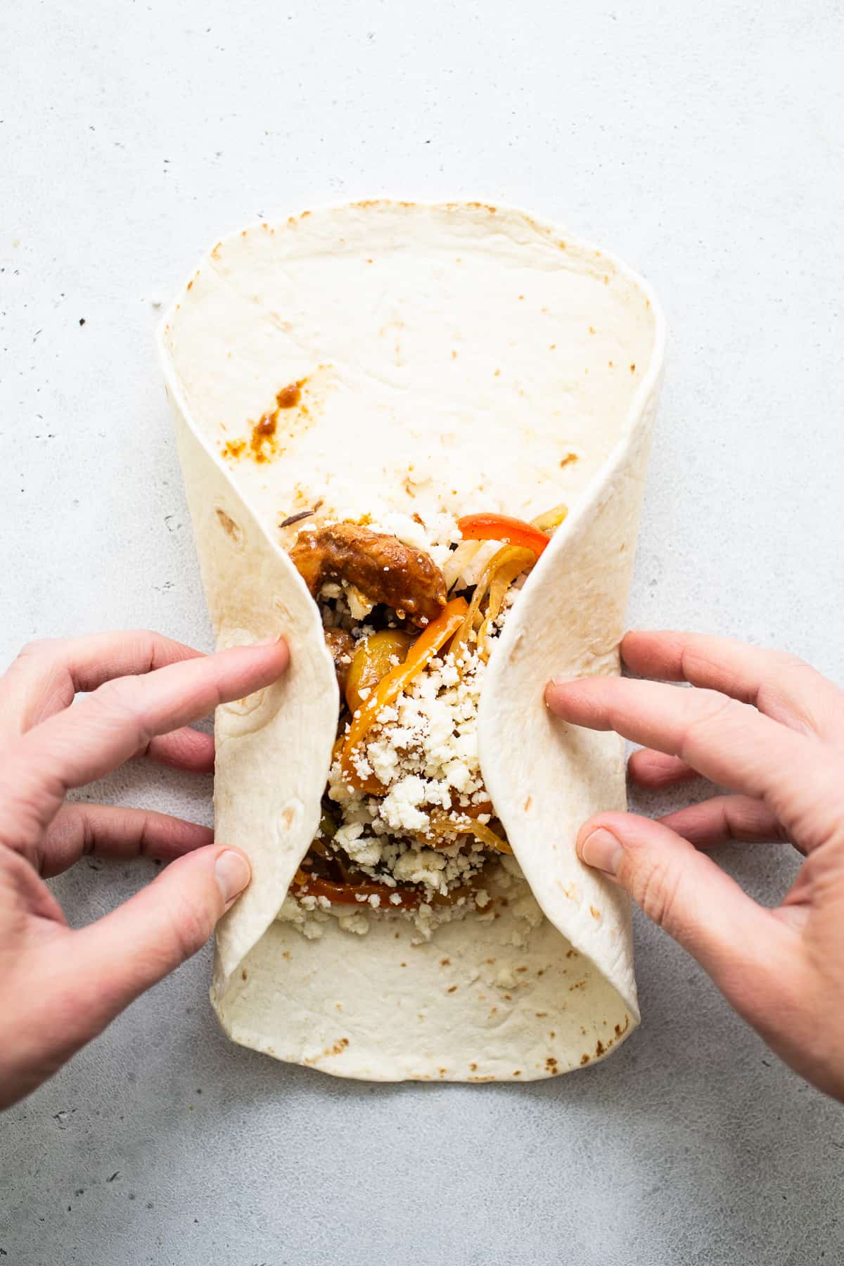 Chicken fajita burrito being rolled up.