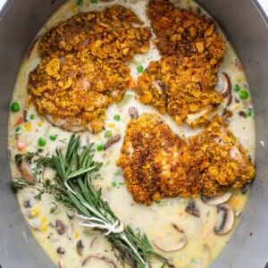 Chicken breasts in a pan with mushrooms and sprigs of rosemary.