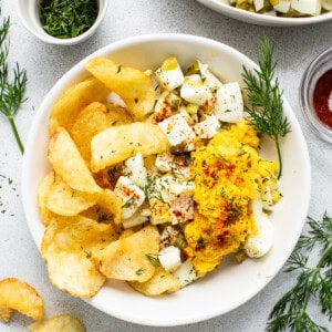 A bowl of potato chips and a bowl of dip.