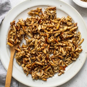 Roasted peanuts on a white plate with a wooden spoon.