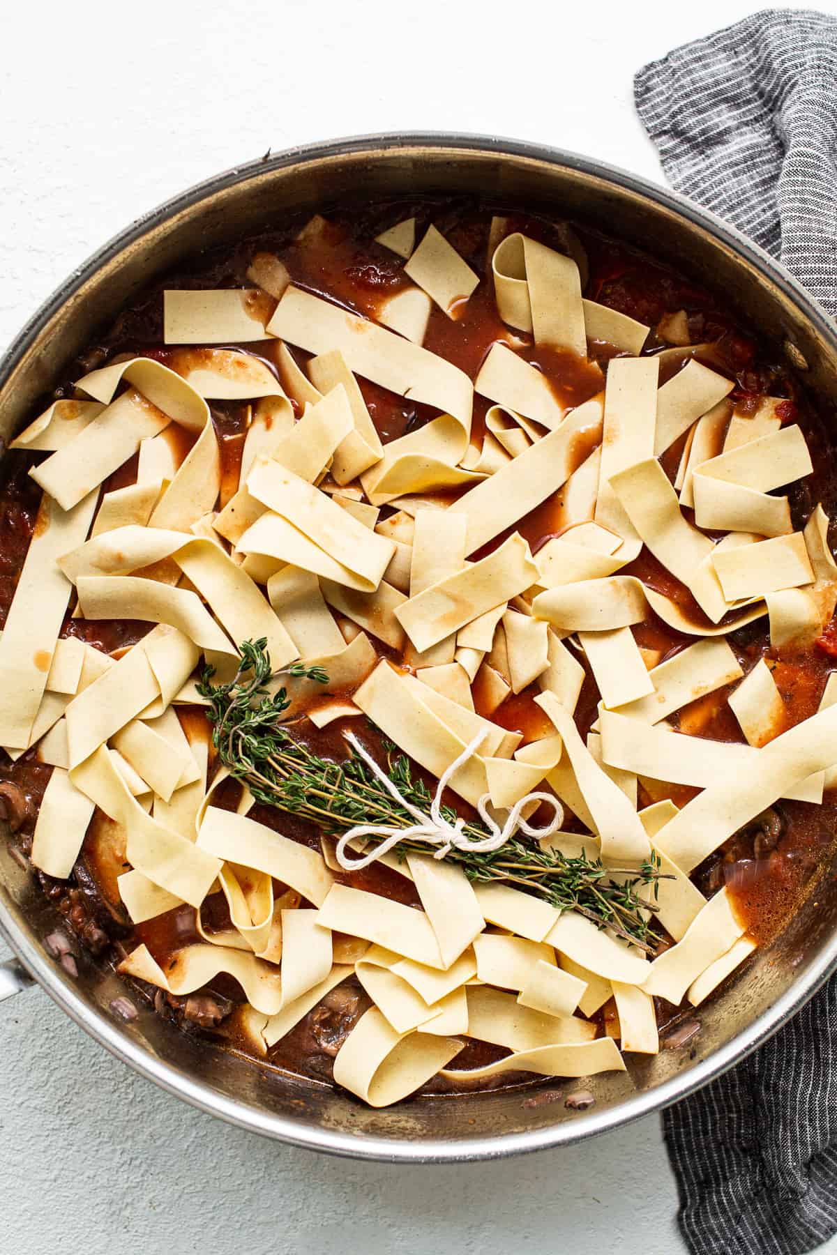 Pappardelle pasta over sauce in a skillet.