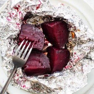 Beets in foil on a plate with a fork.