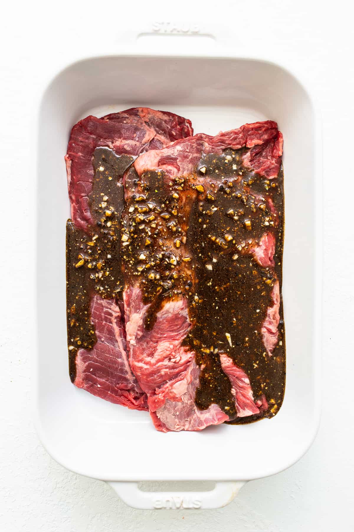 Skirt steak in a dish topped with marinade.