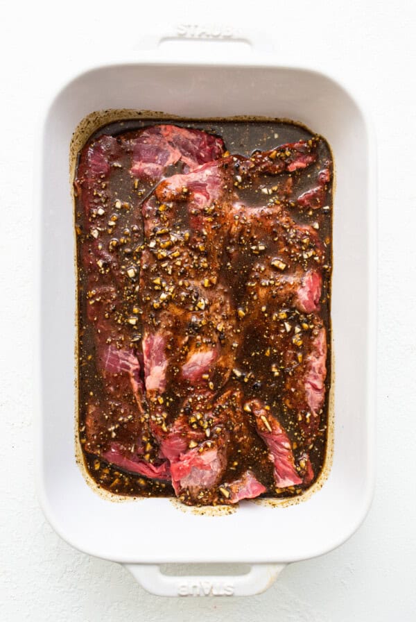 Skirt steak marinating in a baking dish.