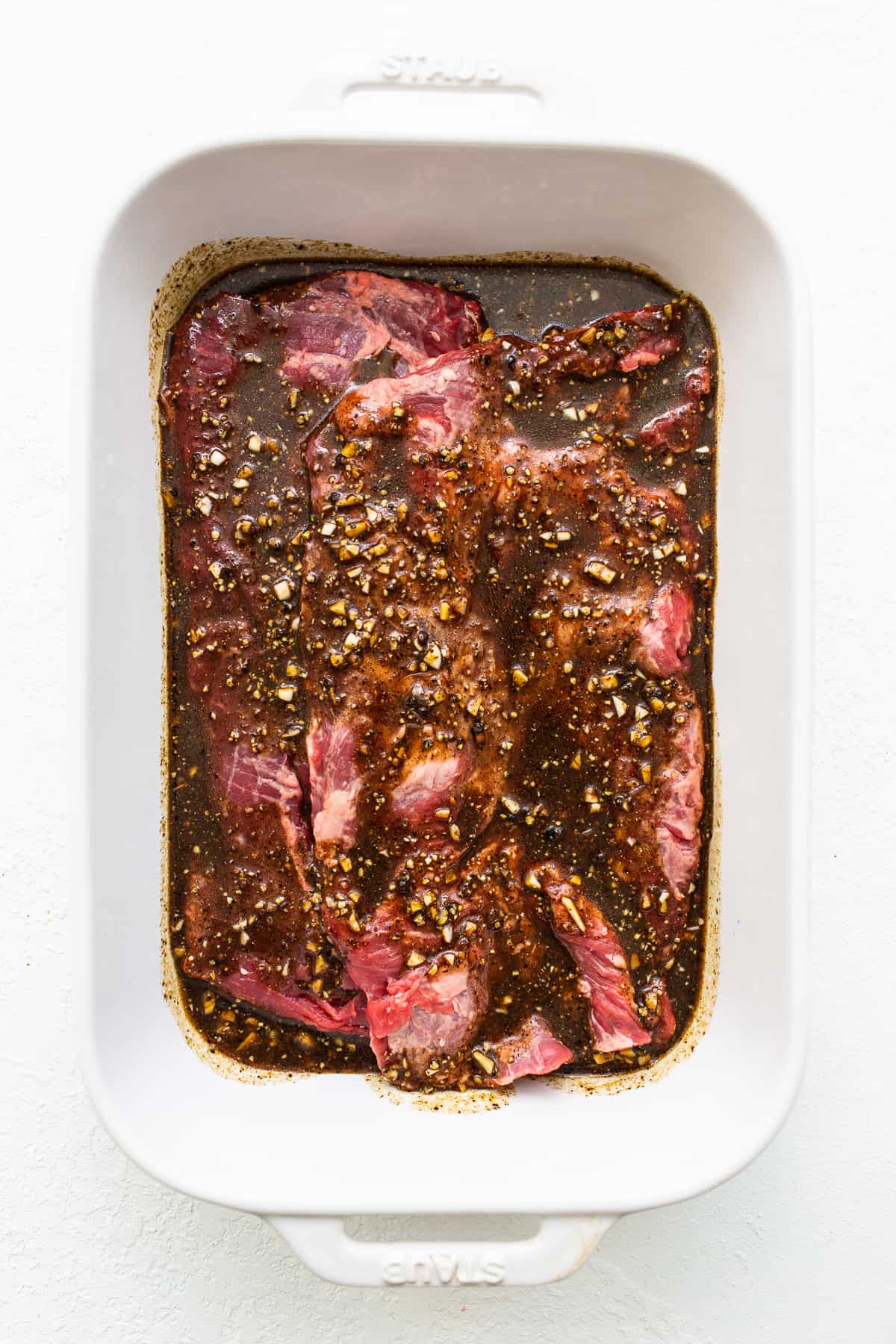 Skirt steak marinating in a baking dish. 