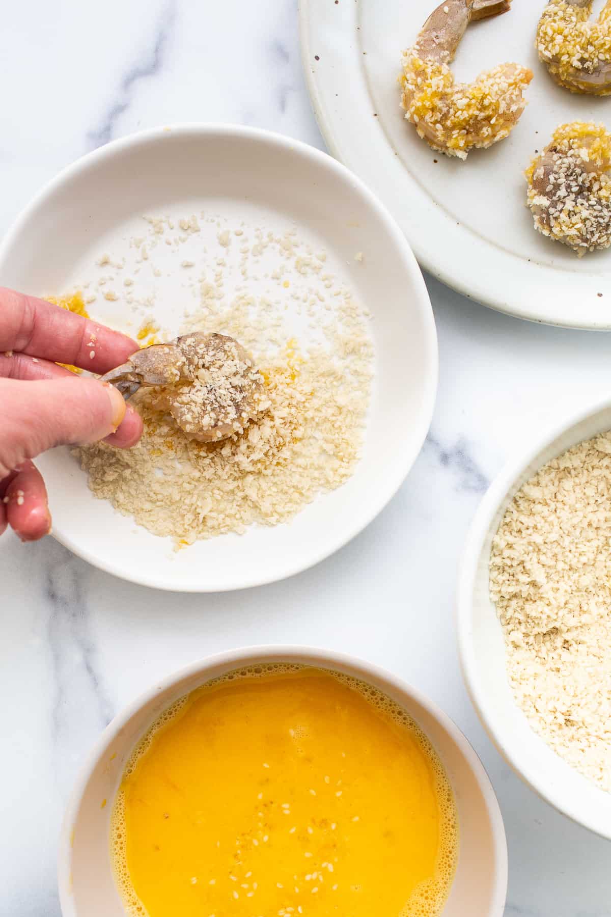 A person drizzling sesame seeds into a bowl of ingredients.