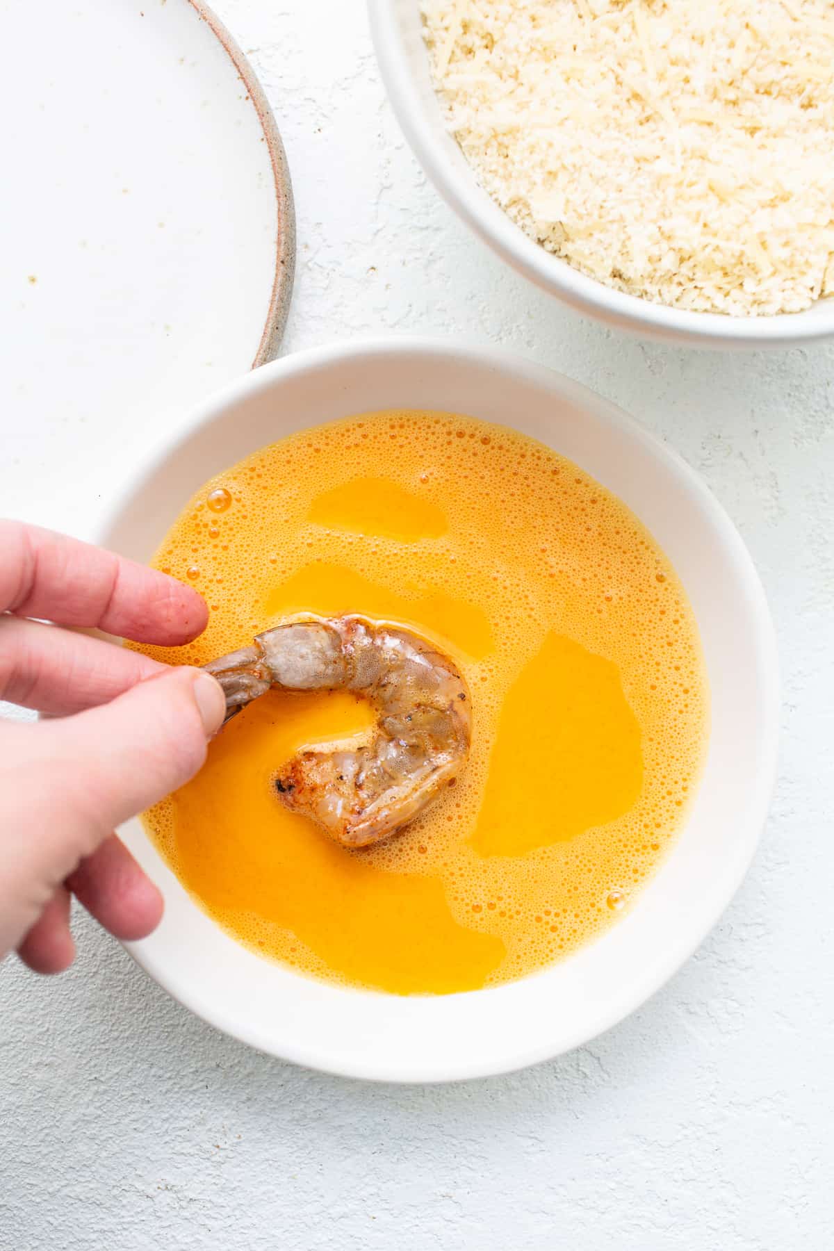 Shrimp being dipped into an egg wash.