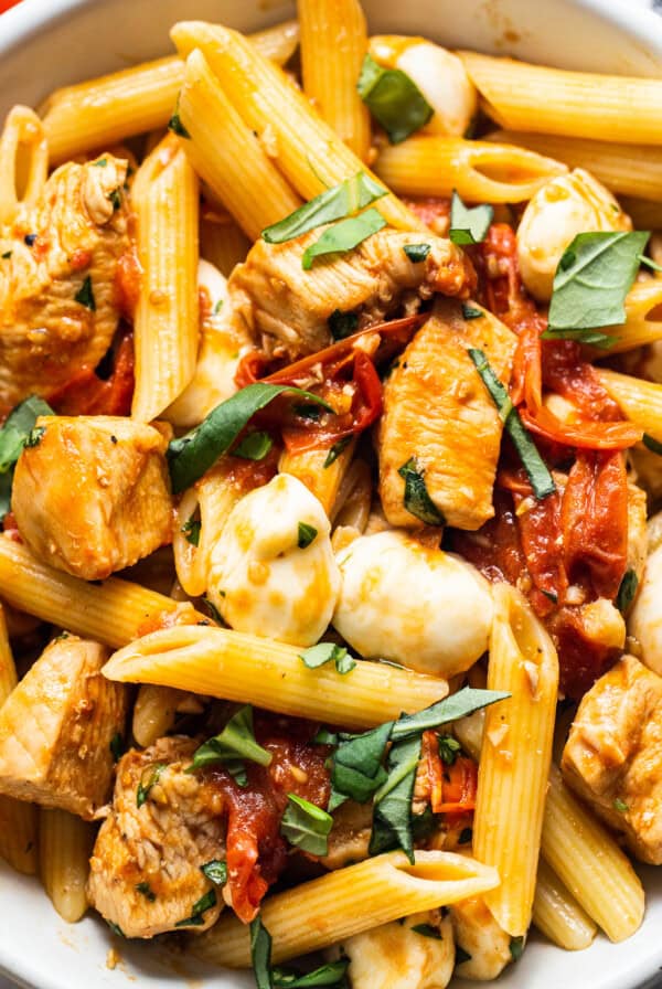 caprese chicken pasta in bowl with fork.