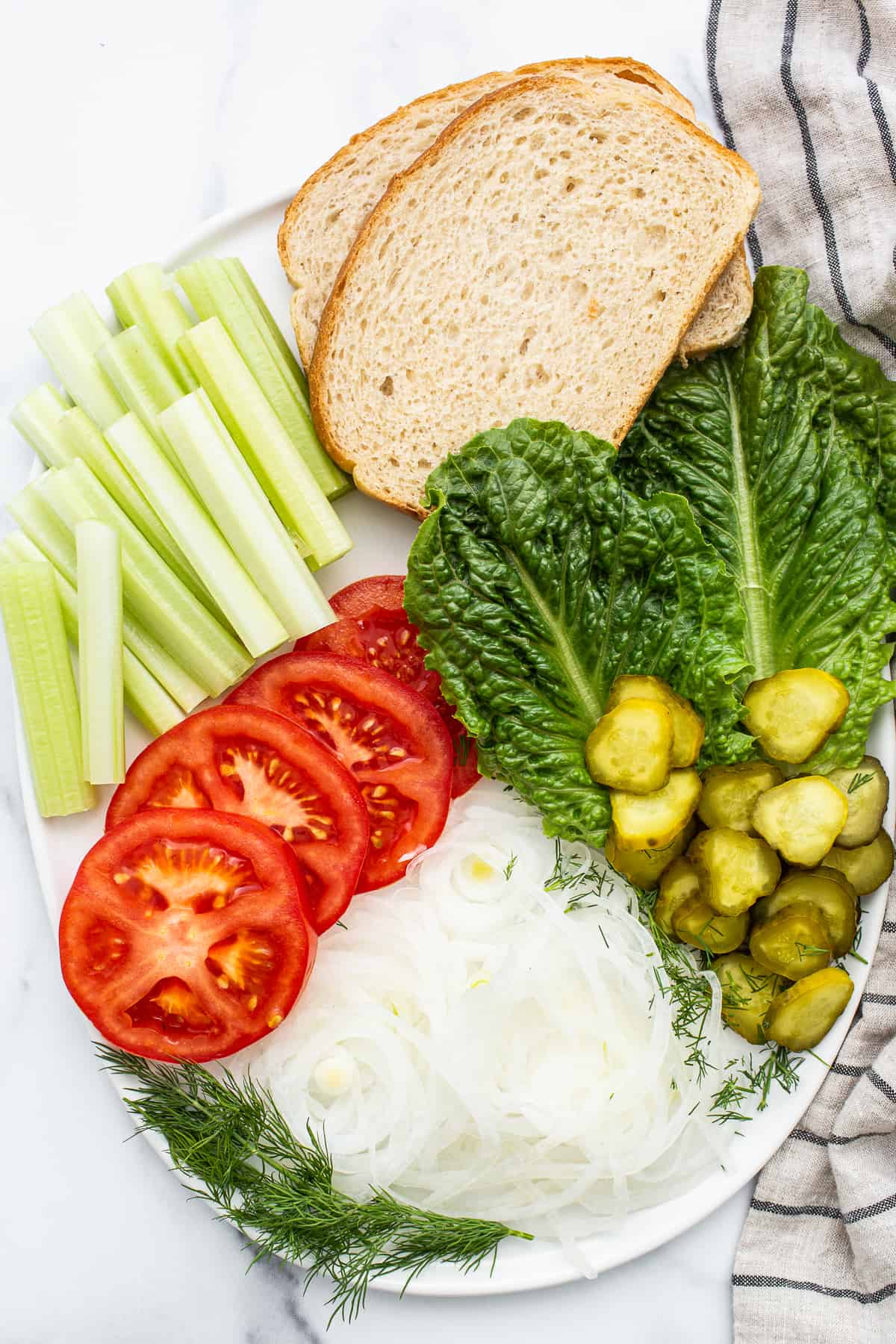 Lettuce, celery, pickles, tomatoes, onion, and bread on a plate. 