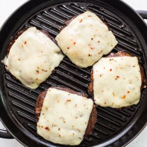 Four cheeseburgers in a grill pan on a white background.