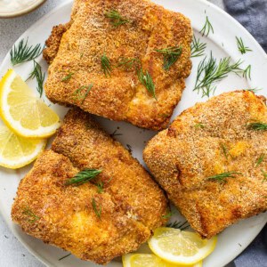 Air fryer fish on a plate with lemon slices.