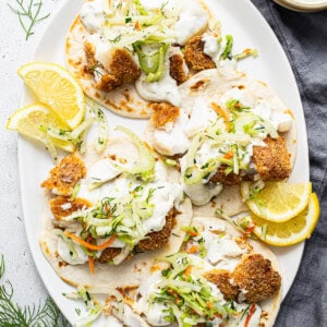 Fish tacos on a white plate with lemon wedges.