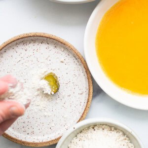 A person is sprinkling flour on a bowl of pickles.