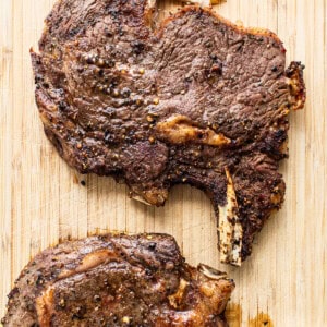 Two steaks on a wooden cutting board.