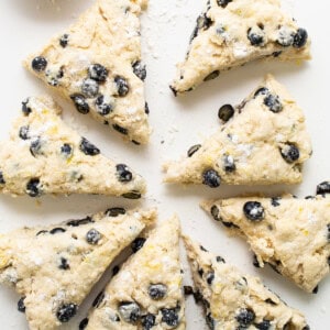 a white plate topped with blueberry scones next to a cup of milk.