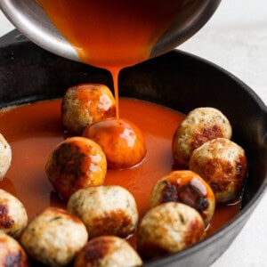 adding sauce to meatballs.