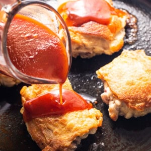 a person pouring ketchup on some food in a skillet.