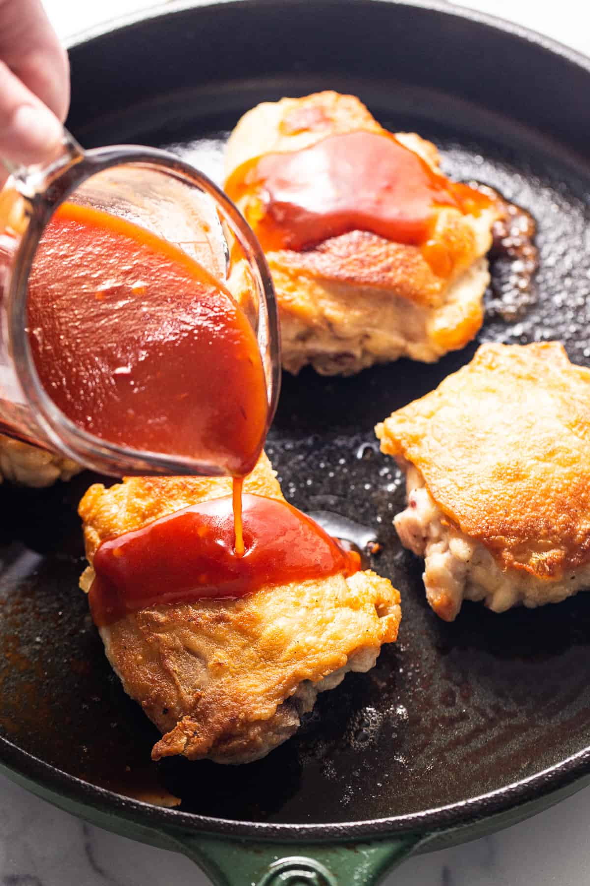 a person pouring ketchup on some food in a skillet.