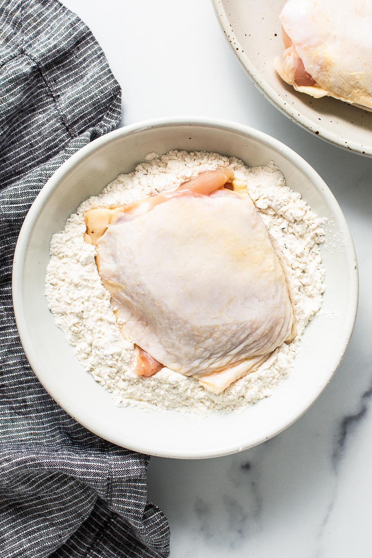 raw chicken thigh being dredged in flour.