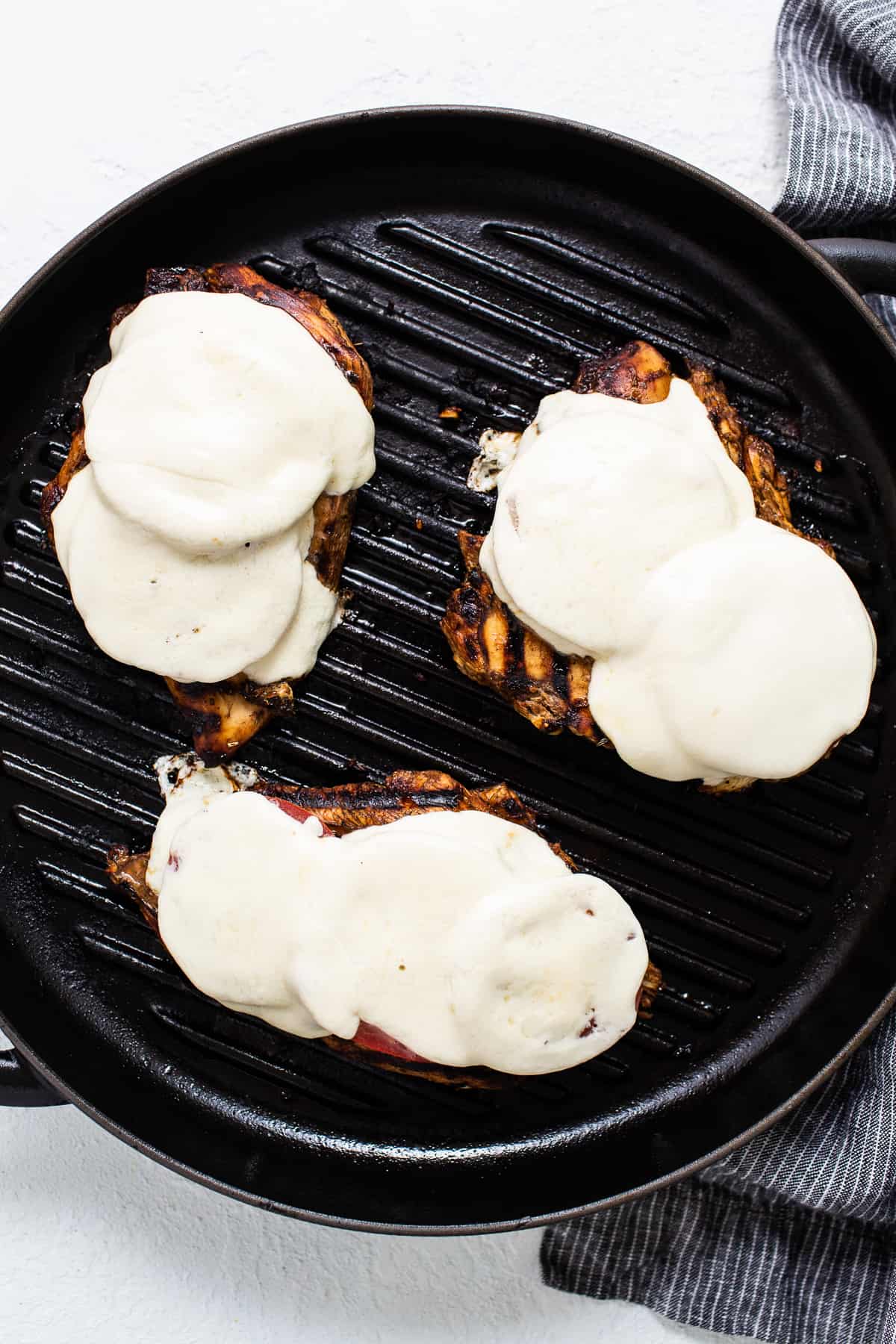 Three grilled chicken breasts with sauce on a grill.