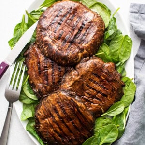 Grilled mushrooms on a plate with spinach and a fork.