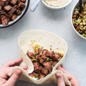 A person holding a burrito filled with beef and vegetables.