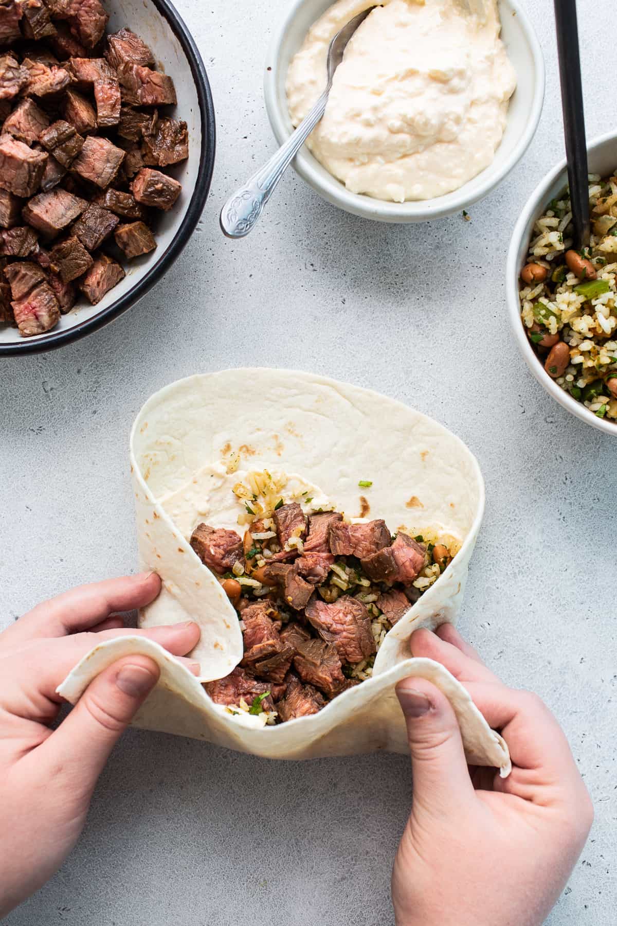 Hands rolling a steak burrito on a counter.